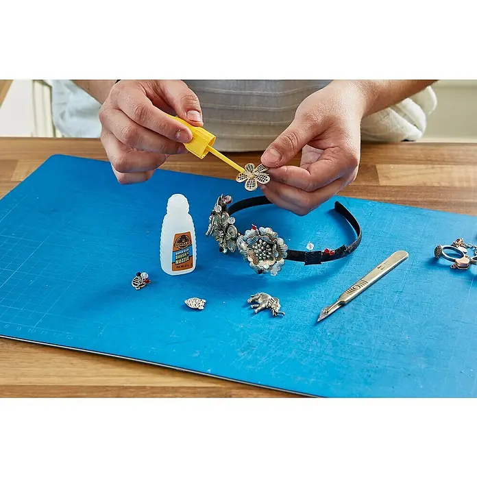 Gorilla Adhesivo instantáneo con pincel y boquilla - 12 g - Manualidades creativas: Primer plano de manos aplicando pegamento con un pincel a un adorno floral decorativo para un proyecto de bricolaje.