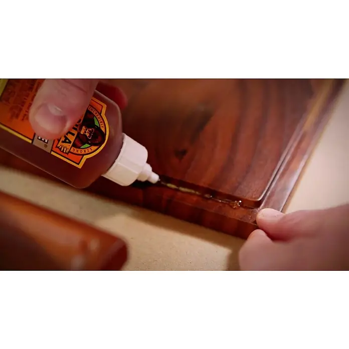 Gorilla Pegamento universal - 60 ml - Un hombre está aplicando pegamento Gorilla a un trozo de madera para repararlo. El pegamento es de color marrón claro y se aplica desde una botella marrón.
