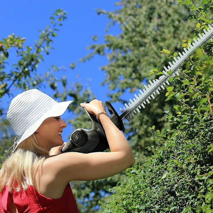 Litheli U20 Akku-Heckenschere - 20 V, Li-Ionen, Ohne Akku, Schnittlänge: 510 cm - Eine Frau benutzt eine Heckenschere, um eine Hecke zu schneiden, wobei der Fokus auf der Heckenschere und der Gartengeräte liegt.