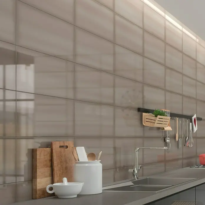 Decocer by Cinca Glow Wandfliese - 25 x 55 cm, Champagner, Glänzend - Detailaufnahme einer Küchenzeile mit grauen Fliesen, Spüle und Küchenutensilien. Die glänzenden Fliesen reflektieren das Licht und verleihen der Küche einen modernen Look.