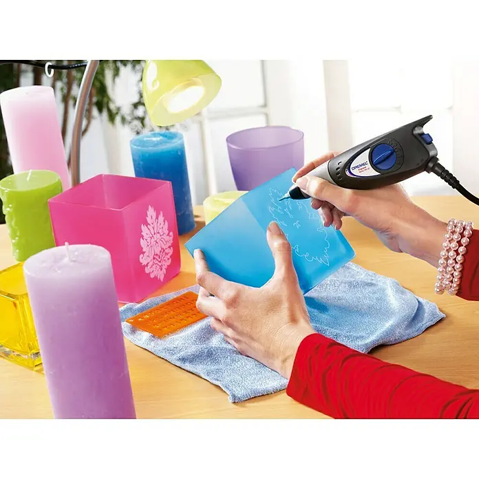 Dremel Graviergerät 290-3 Hobby - 35 W - Handwerker graviert mit einem Dremel Werkzeug ein blaues Objekt, umgeben von bunten Kerzen und Lampen.