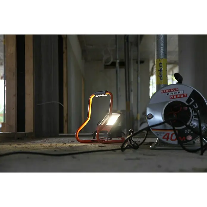 Ledvance LED-Strahler - 30 W, 2.700 lm, 4.000 K, L x B x H: 19 x 22 x 29 cm, IP44 - Eine Baustellenleuchte von Bauhaus Profi Depot und eine Kabelrolle stehen auf dem Boden einer Baustelle.