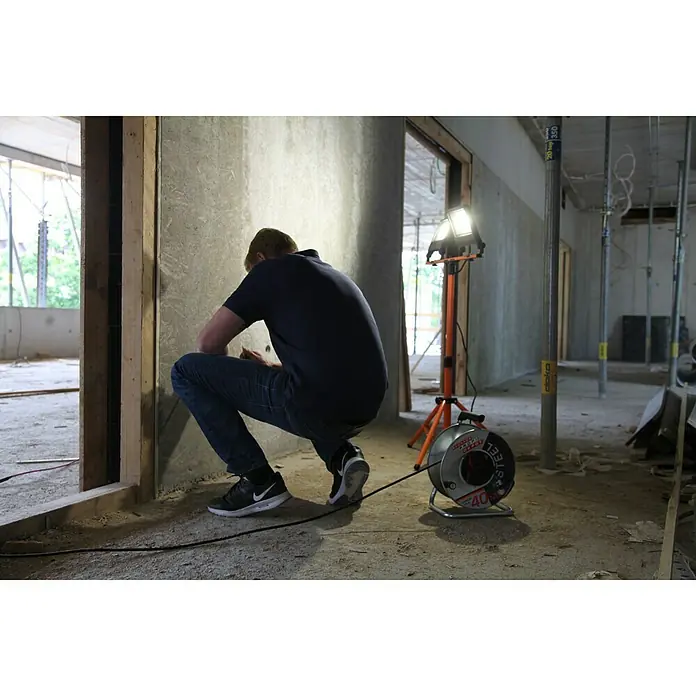 Ledvance LED-Arbeitsleuchte5.400 lm, Lichtfarbe: Kaltweiß, Anzahl Leuchtmittel: 2 Stk. - Ein Bauarbeiter hockt neben einer Stahlspiraleinziehgerät auf einer Baustelle. Das Gerät ist kompakt und für den Einsatz in Rohren und Kanälen konzipiert.