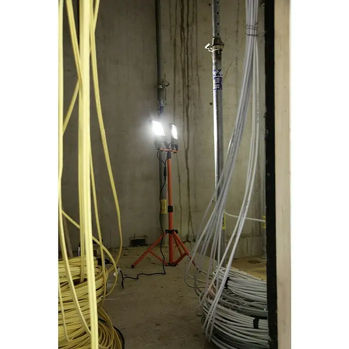 Ledvance LED-Arbeitsleuchte - 5.400 lm, Lichtfarbe: Kaltweiß, Anzahl Leuchtmittel: 2 Stk. - Ein Baustellenbild zeigt eine orangefarbene Baustellenleuchte vor einer Betonwand, umgeben von gelben und grauen Kabeln.