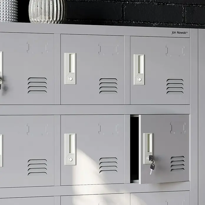Jan Nowak Schließfachschrank Karol - Anzahl Fächer: 18 Stk., Grau - Graue Metallschränke mit Lüftungsschlitzen und Griffen, wobei eine Tür offen steht und einen Schlüssel zeigt. Ideal für sichere Aufbewahrung.