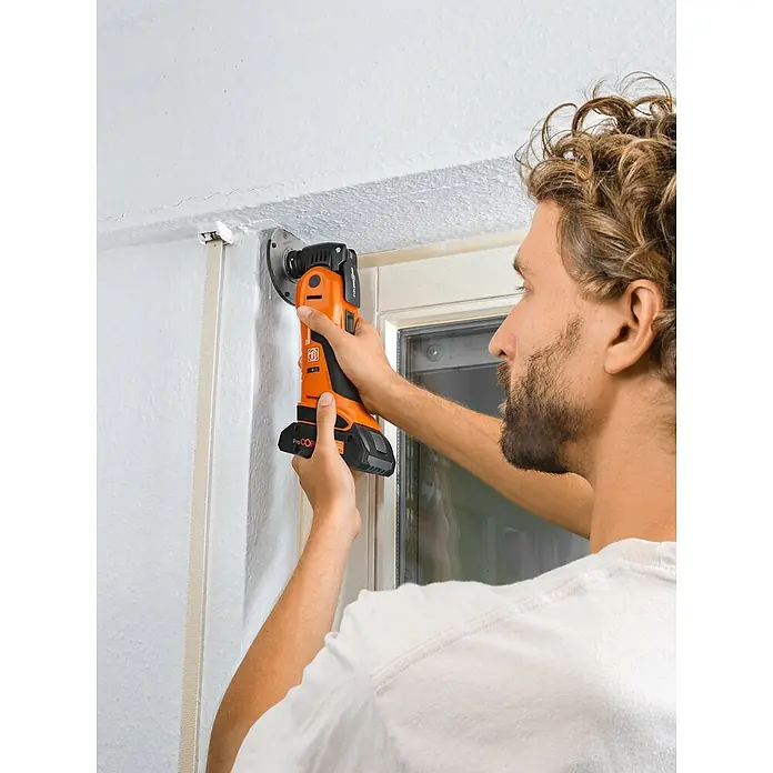 Fein AMPShare 18V Akku-Multifunktionswerkzeug MultiMaster AMM700 MAX AS - 18 V, Ohne Akku, Leerlaufschwingzahl: 10.000 /min - 19.500 /min - Ein Mann benutzt ein orangefarbenes, oszillierendes Multifunktionswerkzeug, um an einem Fensterrahmen zu arbeiten. Das Werkzeug ist kabellos mit Akku.