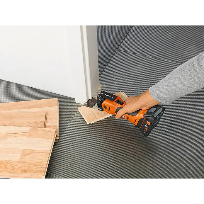 Fein AMPShare 18V Akku-Multifunktionswerkzeug MultiMaster AMM700 MAX AS - 18 V, Ohne Akku, Leerlaufschwingzahl: 10.000 /min - 19.500 /min - Multifunktionswerkzeug beim Kürzen einer Holztür mit Holzboden und einem Arm, der das Werkzeug hält.