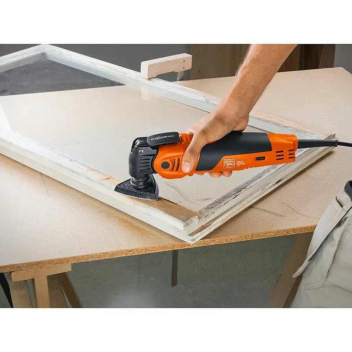 Fein MultiMaster Elektro-Multifunktionswerkzeug MULTIMASTER MM700 MAX TOP L-BOXX SET - 450 W, STARLOCK-Max-System - Handwerker schleift Fensterrahmen mit einem oszillierenden Fein Multimaster 700 Elektrowerkzeug, für präzise Renovierungsarbeiten.