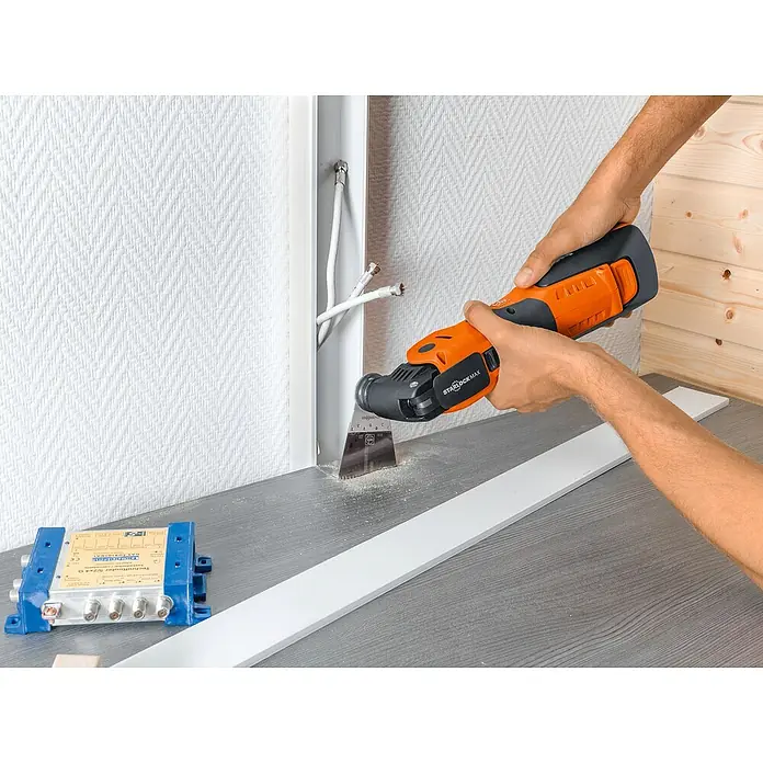 Fein Starlock Plus Hoja de sierra E-Cut Precision - 65 x 50 mm, 3 ud. - Un hombre usa una multiherramienta oscilante para cortar un agujero en una pared para pasar cables.