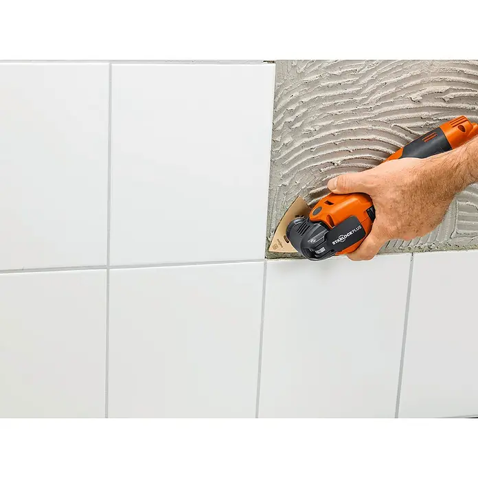 Fein Starlock Hartmetall-Raspel - Breite: 80 mm - Ein Mann entfernt mit einem oszillierenden Multitool Fliesen von einer Wand, um ein beschädigtes Badezimmer zu reparieren.