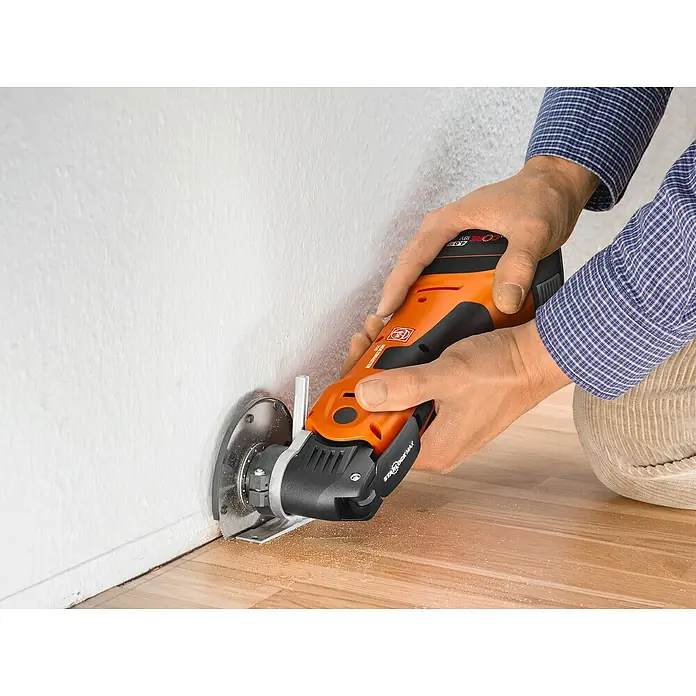 Fein AMPShare 18V Akku-Multifunktionswerkzeug MultiMaster AMM700 MAX AS - 18 V, Ohne Akku, Leerlaufschwingzahl: 10.000 /min - 19.500 /min - Ein Mann benutzt ein FEIN oszillierendes Elektrowerkzeug, um einen Sockel an einer Wand zu bearbeiten. Das Werkzeug ist orange und schwarz.