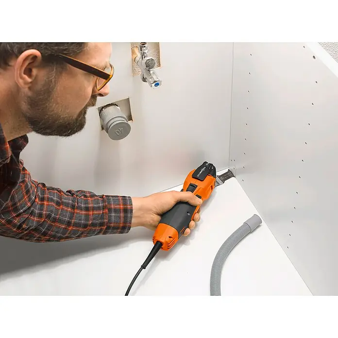 Fein MultiMaster Elektro-Multifunktionswerkzeug MultiMaster MM500 Plus TOP L-BOXX SET - 350 W, STARLOCK-Plus-System - Eine orangefarbene Multifunktionswerkzeug schneidet in einer Ecke einer weißen Küchenzeile. Der Installateur mit Schutzbrille ist dabei zu sehen.