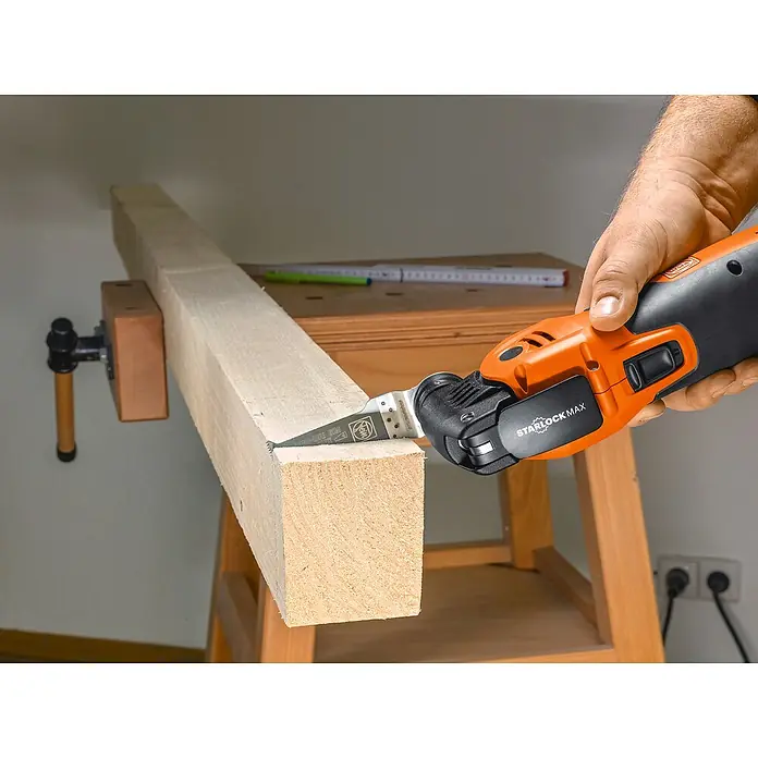 Fein MultiMaster Elektro-Multifunktionswerkzeug MULTIMASTER MM700 MAX TOP L-BOXX SET - 450 W, STARLOCK-Max-System - Ein Mann benutzt ein oszillierendes Multifunktionswerkzeug zum Schneiden eines Holzstücks, das in einem Schraubstock befestigt ist.