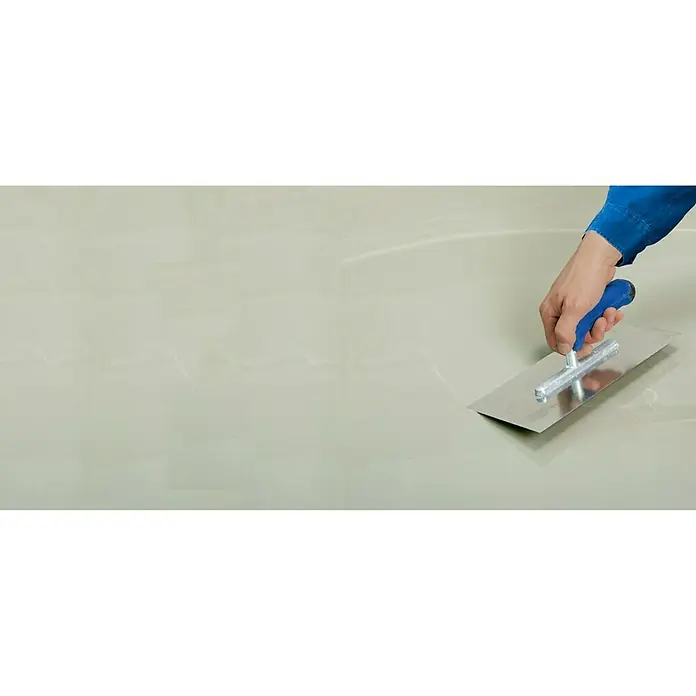 Knauf Flexdicht - 15 kg - Eine Hand glättet eine Oberfläche mit einer Glättkelle, um eine ebene Fläche zu schaffen. Werkzeug für Bau und Handwerk im Einsatz.