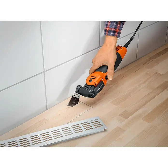 Fein MultiMaster Elektro-Multifunktionswerkzeug MULTIMASTER MM700 MAX TOP L-BOXX SET - 450 W, STARLOCK-Max-System - Eine oszillierende Säge schneidet ein Stück Holz aus, um eine Lüftungsabdeckung anzubringen. Das Werkzeug ist orange und schwarz.