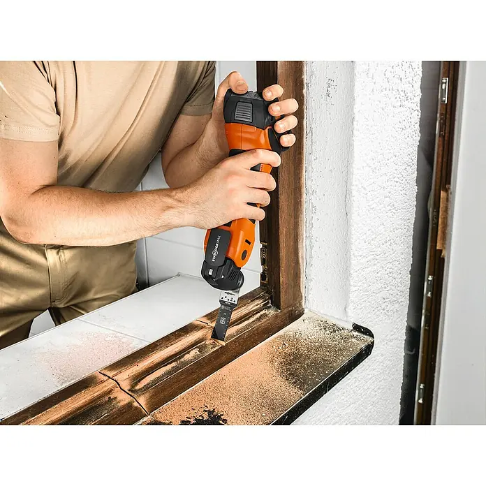 Fein AMPShare 18V Akku-Multifunktionswerkzeug MultiMaster AMM700 MAX AS - 18 V, Ohne Akku, Leerlaufschwingzahl: 10.000 /min - 19.500 /min - Ein Mann verwendet ein oszillierendes Multifunktionswerkzeug, um Holz an einem Fensterrahmen zu schneiden.