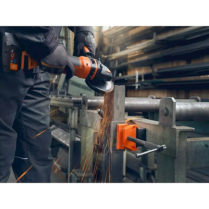 Fein Schraubstock VersaMAG - Spannweite: 108 mm, Metall - Ein Mann benutzt einen FEIN Akku-Winkelschleifer zum Schleifen von Metall in einer Werkstatt, wodurch Funken entstehen.