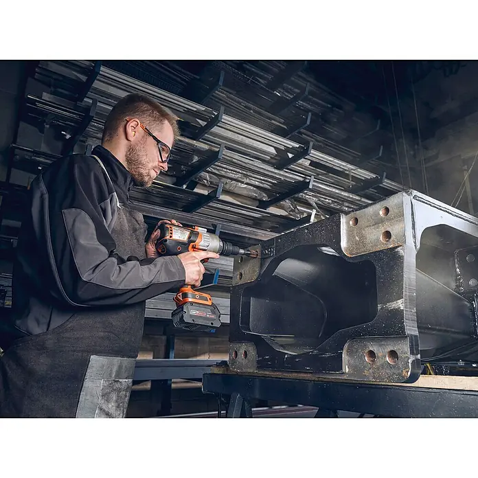 Fein Werkzeughalter - Passend für: 3/4" Außenvierkant ISO 1174-2 F 20, 1 Stk. - Ein Mann mit Schutzbrille arbeitet mit einem orangefarbenen Akku-Bohrschrauber an einem schwarzen Metallrahmen in einer Werkstatt.