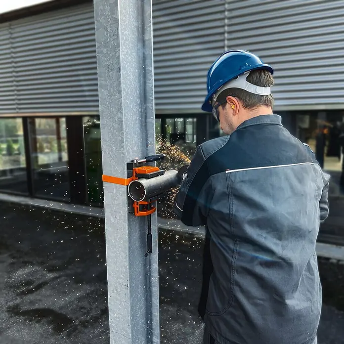 Fein Schraubstock VersaMAG - Spannweite: 108 mm, Metall - Ein Arbeiter mit Schutzhelm schneidet ein Rohr mit einer Rohrschneidemaschine, die an einem Metallpfosten befestigt ist. Funken fliegen beim Schneiden.