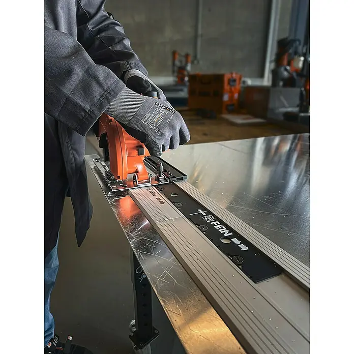Fein AMPShare 18V Akku-Handkreissäge AHKS 18-57 AS N00 - 18 V, Ohne Akku, Durchmesser Sägeblatt: 150 mm, 1.300 U/min - 2.800 U/min - Bild einer FEIN Tauchsäge mit Führungsschiene im Einsatz, die auf einer Werkbank liegt. Eine Person mit Schutzhandschuhen bedient die Säge.