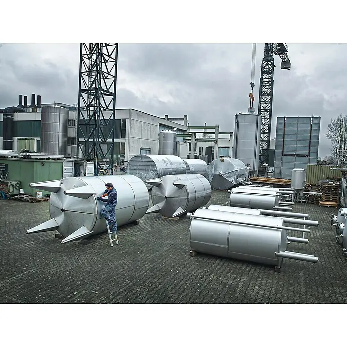 Fein AMPShare 18V Akku-Geradschleifer AGSZ 18-90 LBL AS - 18 V, Ohne Akku, Leerlaufdrehzahl: 2.900 U/min - 9.000 U/min - Mann arbeitet an einem metallenen Druckbehälter mit konischen Füßen, während im Hintergrund weitere Behälter und Industrieanlagen zu sehen sind.