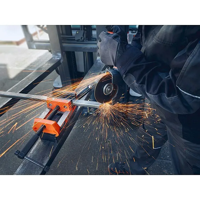 Fein Schraubstock VersaMAG - Spannweite: 108 mm, Metall - Arbeiter schneidet mit einer Flex Metall, Funken sprühen. Die Flex und die Sicherheitsausrüstung des Arbeiters sind gut sichtbar.
