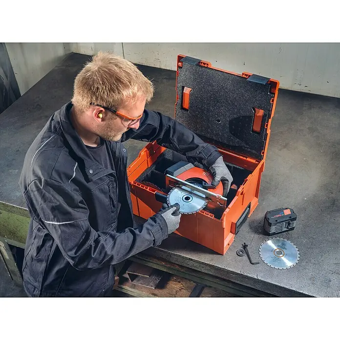 Fein AMPShare 18V Akku-Handkreissäge AHKS 18-57 AS N00 - 18 V, Ohne Akku, Durchmesser Sägeblatt: 150 mm, 1.300 U/min - 2.800 U/min - Ein Handwerker wechselt eine Sägeblatt einer Akku-Kreissäge in einem orangefarbenen Werkzeugkoffer.