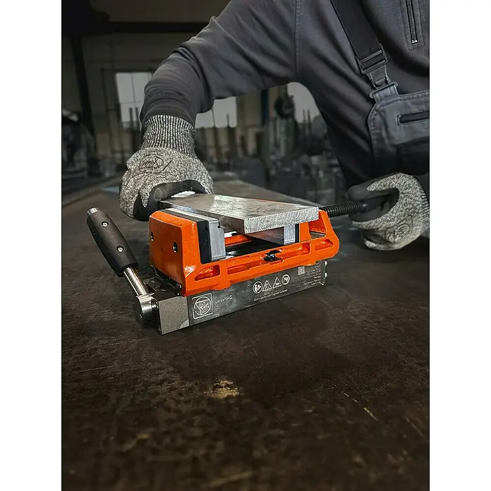 Fein AMPShare 18V Akku-Winkelschleifer CCG 18-125-12 AS - Ohne Akku, Durchmesser Scheibe: 125 mm - Nahaufnahme eines FEIN VersaMAG Magnetspannblocks in Aktion, bedient von einem Arbeiter mit Schutzhandschuhen.
