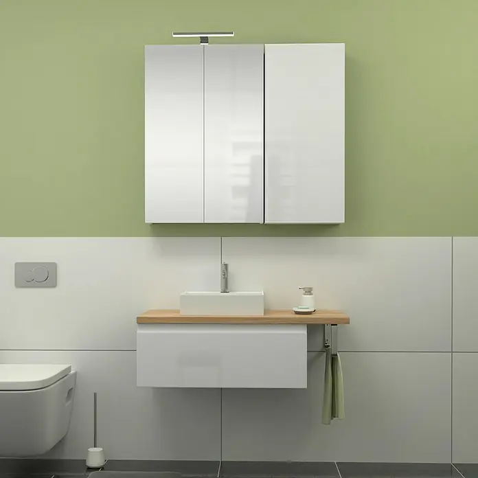 Camargue Espacio Badmöbel-Set i133 - 100 cm, Gama weiß glänzend - Helles Badezimmer mit weißem Waschbeckenunterschrank, einem Spiegelhängeschrank und WC. Die Wand ist oben grün und unten weiß gefliest.
