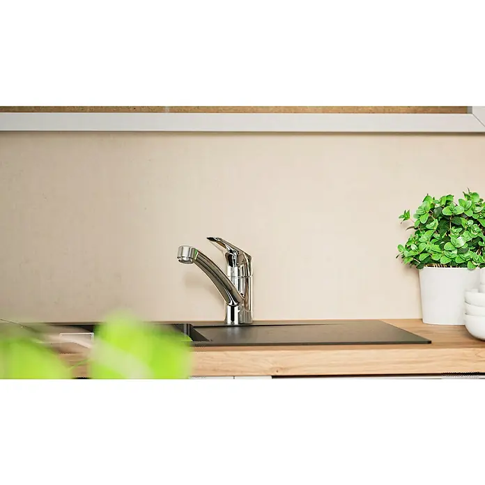 Hansgrohe Grifo de cocina Logis 120 - Cromo, Brillante - Primer plano de un grifo de cocina brillante sobre una encimera, junto a una planta y tazones apilados. Tonos claros dominan.