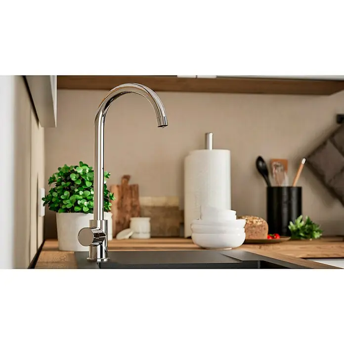 Grohe Spültischarmatur Blue Home Mono - Höhe: 37,9 cm, C-Auslauf, Chrom, Glänzend, Schwenkbar - Nahaufnahme eines modernen Chrom-Wasserhahns vor Küchendekor. Der schlanke Wasserhahn ist ein Blickfang, umgeben von Grünpflanzen und Küchenutensilien.