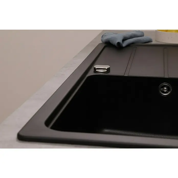 Respekta Einbauspüle Austin - 100 x 50 cm, Schwarz, Anzahl Becken: 1 Stk. - Nahaufnahme einer modernen schwarzen Küchenspüle mit Abtropffläche und einem blauen Tuch auf der Arbeitsfläche. Elegantes Design für jede Küche.