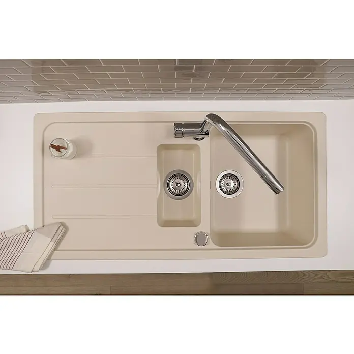 Respekta Einbauspüle Austin - 100 x 50 cm, Vanille, Anzahl Becken: 1,5 Stk. - Nahaufnahme einer beigefarbenen Küchenspüle mit Abtropffläche, Spülbecken und Armatur vor einem Hintergrund aus Ziegeln.