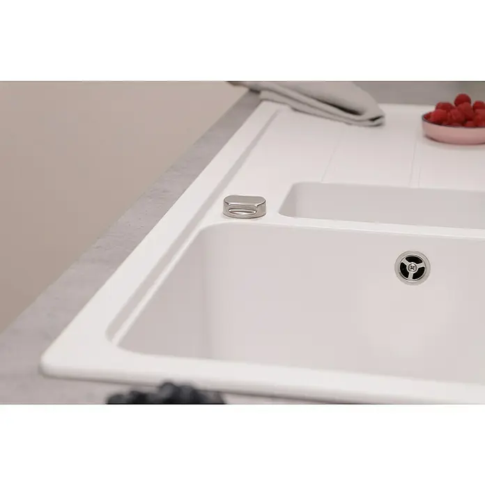 Respekta Einbauspüle Austin - 100 x 50 cm, Weiß, Anzahl Becken: 1,5 Stk. - Nahaufnahme einer weißen Küchenspüle mit Abfluss, einem silbernen Knopf und frischen Beeren als Dekoration auf der Arbeitsfläche.