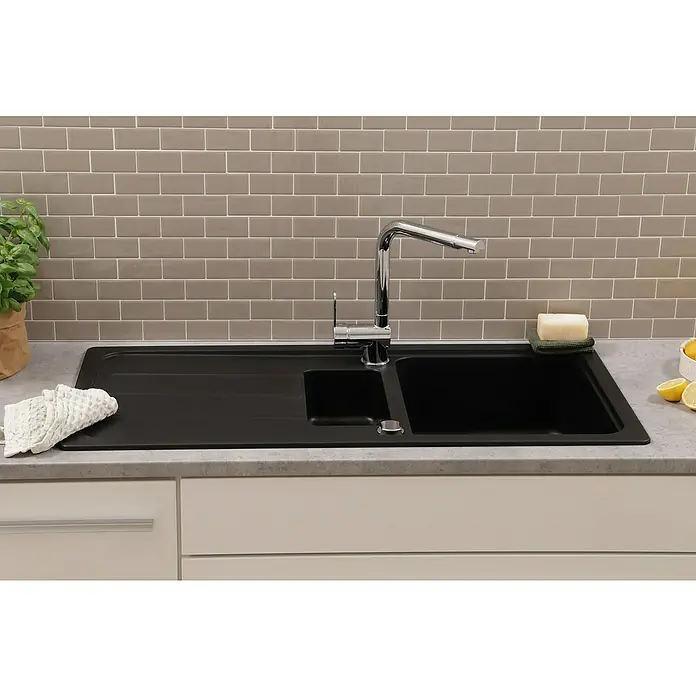 Respekta Einbauspüle Austin - 100 x 50 cm, Schwarz, Anzahl Becken: 1,5 Stk. - Nahaufnahme einer schwarzen Spüle mit Abtropffläche, einem Hahn und Küchenutensilien vor einer grauen Backsteinwand.