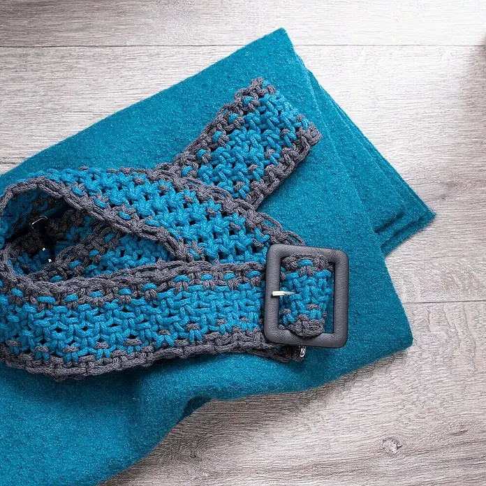 Glorex Wolle Makramee-Cotton - Türkis, Durchmesser: 2 mm, 250 g - Eine gehäkelte Gürtelkomposition in Blau- und Grautönen, ergänzt durch eine Schnalle, die auf einem türkisfarbenen Stoff platziert ist.