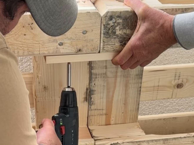 An zwei Paletten wird an der Innenseite eine Holzlatte angeschraubt, die als Verbindungsstück dient