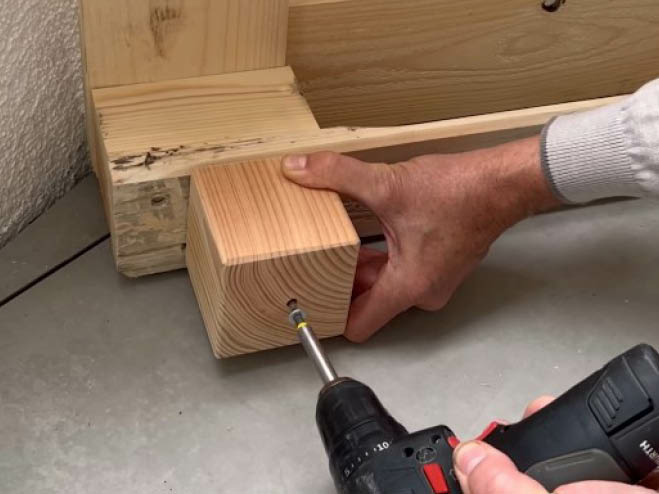 Ein Holzklotz wird an der Unterseite der Palette geschraubt und dient als Möbelfuß