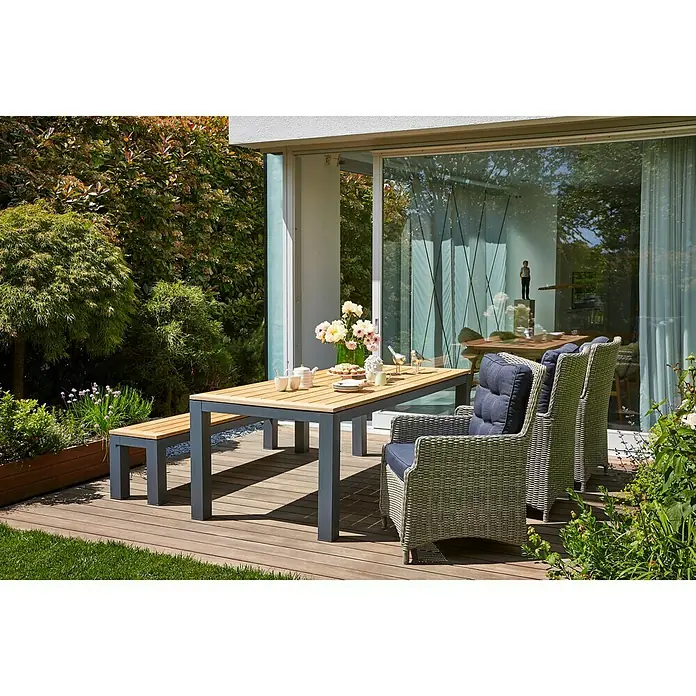 Sunfun Gartentisch Lynn - L x B x H: 220 x 100 x 76 cm, Akazie, Aluminium, Teakbraun, Anthrazit - Elegantes Gartenmöbel-Set mit Tisch, Bank und Korbstühlen mit blauen Kissen auf einer Holzterrasse. Perfekt für entspannte Stunden im Freien.