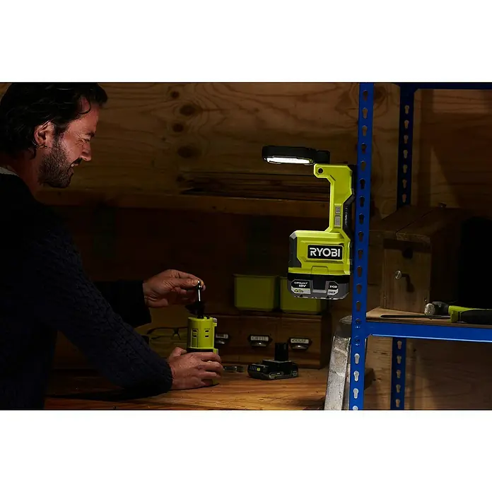 Ryobi ONE+ LED-Arbeitsleuchte RMTL18-0 - 1.500 lm, Ohne Akku - Ein Mann arbeitet mit einem Ryobi-Werkzeug in einer Werkstatt, beleuchtet von einer Ryobi-Arbeitsleuchte, die an einem Regal befestigt ist.