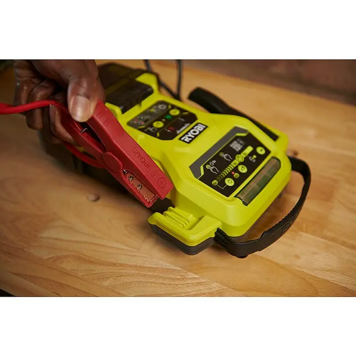Ryobi ONE+ Starthilfegerät RJSC18-0 - Ohne Akku, Ladestrom: 30 A - Ein tragbarer Ryobi-Batterie-Booster mit einer roten Klemme wird vor einem hellgrünen Booster auf einem Holztisch angezeigt.