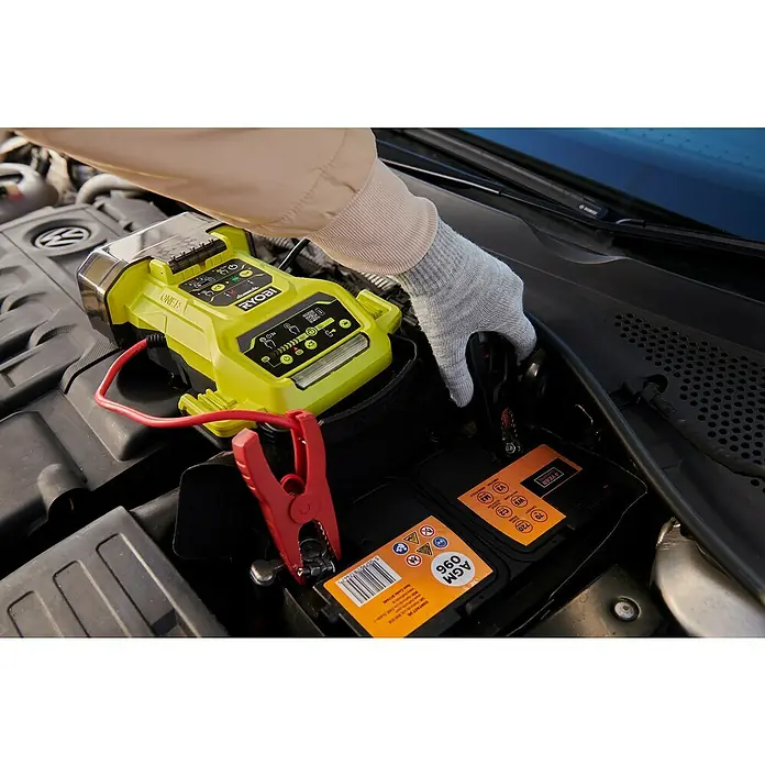Ryobi ONE+ Starthilfegerät RJSC18-0 - Ohne Akku, Ladestrom: 30 A - Autobatterie wird mit einem gelben RYOBI-Ladegerät und roten Klemmen überbrückt, während eine Hand die Verbindung überwacht.