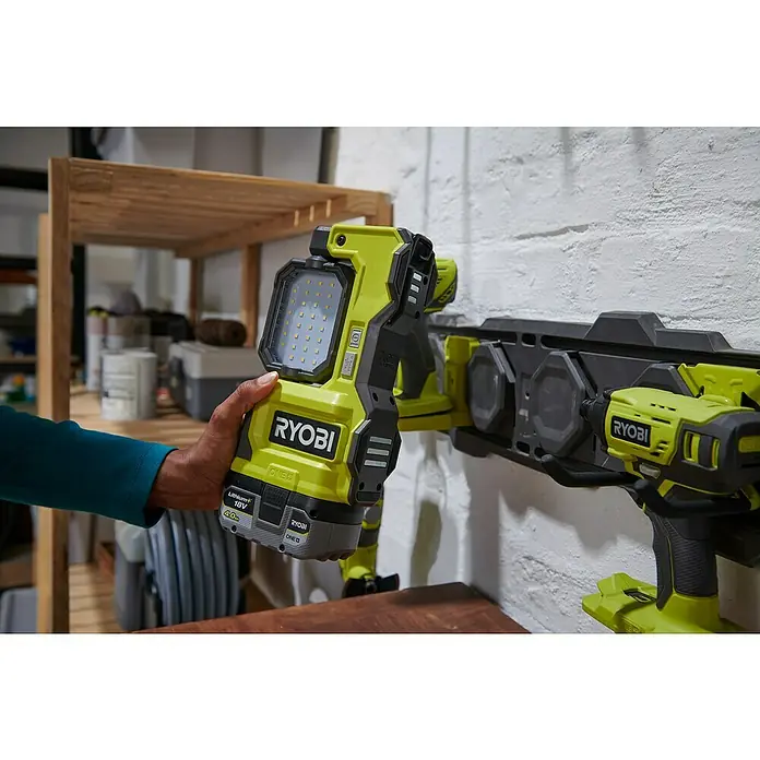 Ryobi ONE+ LED-Arbeitsleuchte RMTL18-0 - 1.500 lm, Ohne Akku - Ryobi Werkstatt-Szene mit Akkulampe in der Hand und Werkzeugen an einer Wandhalterung.