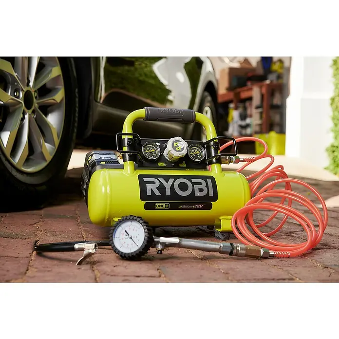 Ryobi ONE+ Akku-Kompressor PRO - 18 V, 3,8 l, 8,3 bar, Ohne Akku - Nahaufnahme eines tragbaren, gelben Ryobi ONE+ 18V Luftkompressors mit Manometer, Schlauch und Zubehör auf einem gepflasterten Untergrund.