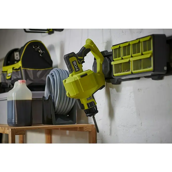 Ryobi ONE+ Akku-Rohrreinigungsgerät RDA18-0 - Ohne Akku - Ein Ryobi-Werkzeug, an einer Wandhalterung befestigt, daneben Werkzeugkästen und auf einem Regal eine Flasche und ein Schlauch.