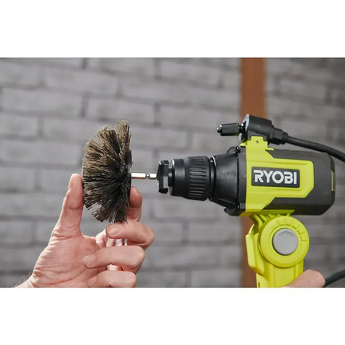 Ryobi Ersatzbürstenkopf RACLRH110 - Hart, Passend für: Ryobi Akku-Reinigungsbürste RSCR4 - Eine Bohrmaschine der Marke Ryobi mit einer runden Drahtbürste, die von einer Hand gehalten wird, vor einer Backsteinmauer.