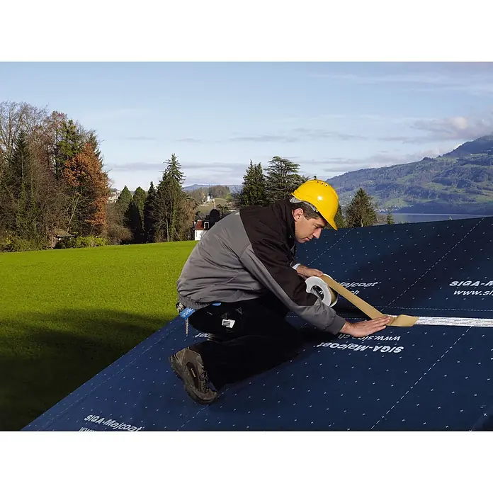Siga Klebeband Wigluv 60 - 15 m x 60 mm, Kunststoff - Ein Bauarbeiter mit gelbem Helm verklebt SIGA-Majcoat Dichtungsbahn auf einem Dach, um es wetterfest zu machen.