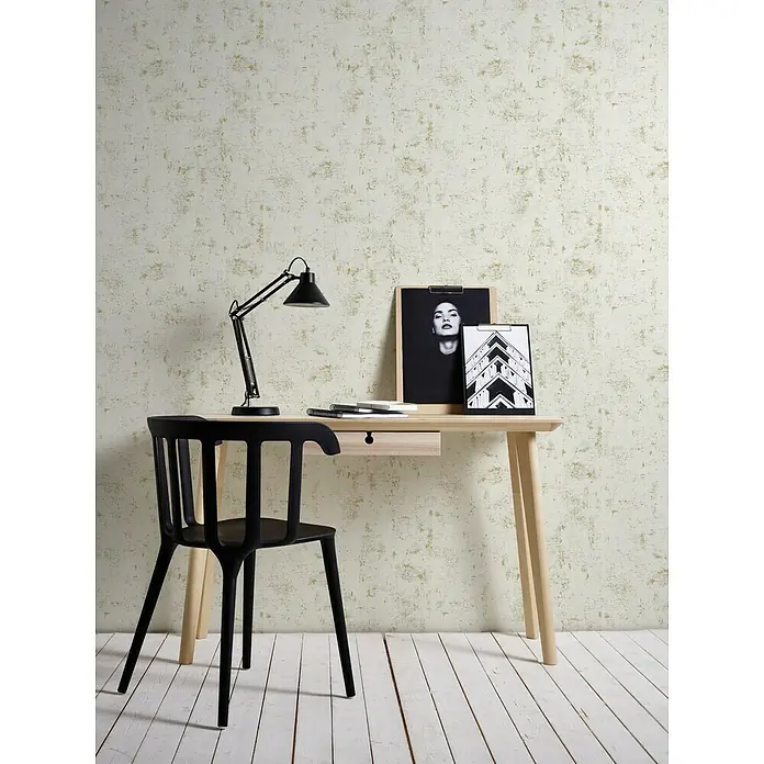 A.S. Création Trendwall Vliestapete - Beige/Gold/Metallic, Betonoptik, 10,05 x 0,53 m - Ein minimalistischer Arbeitsbereich mit einem hellen Holzschreibtisch, einer schwarzen Lampe und einem schwarzen Stuhl vor einer strukturierten Wand.