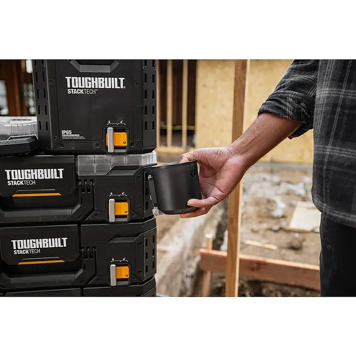 ToughBuilt StackTech Portavaso con vaso térmico - 591 ml, Acero inoxidable, Negro - Un hombre adjunta una taza de herramientas ToughBuilt StackTech a un sistema de almacenamiento de herramientas modular. El diseño resistente es ideal para obras.
