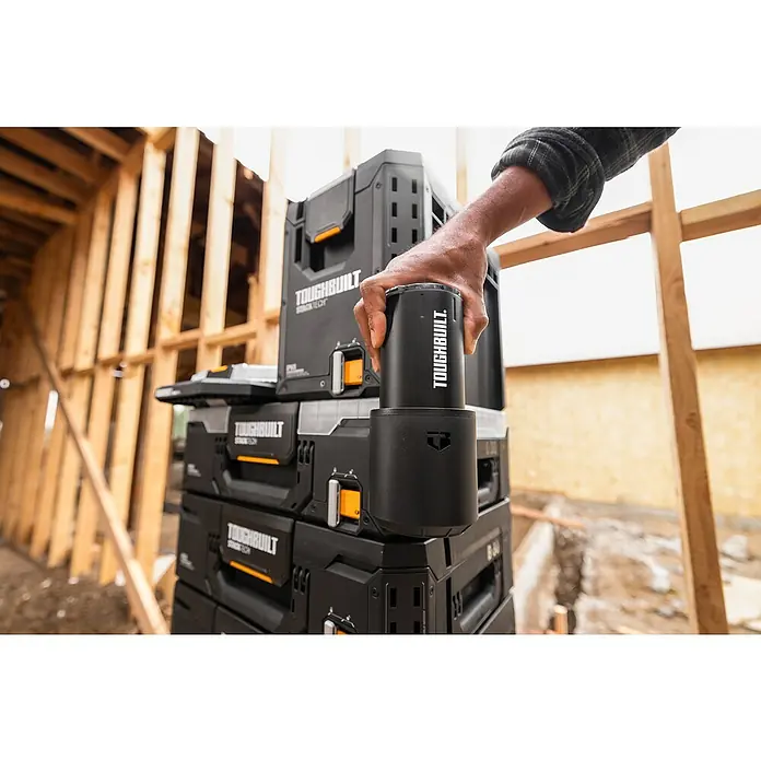 ToughBuilt StackTech Portavaso con vaso térmico - 591 ml, Acero inoxidable, Negro - Una mano sostiene una taza negra ToughBuilt sobre una pila de cajas de herramientas ToughBuilt. Equipo de construcción profesional en uso.